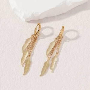 Elegant gold feather earrings with long chain dangles on a white stone background