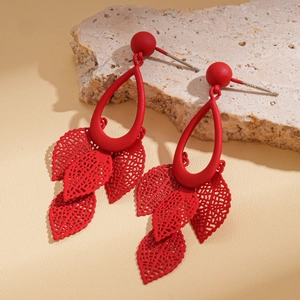 Macro detail of red matte drop earrings with hollow leaf tassels on a natural stone
