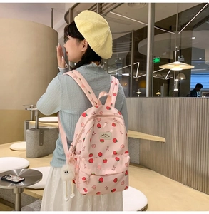 Model wearing a pink strawberry print backpack with a cute white plush ball charm