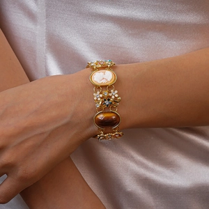 Nahaufnahme eines Vintage-Goldarmbands mit Cameo, Emaille-Blumen und Harzstein am Handgelenk