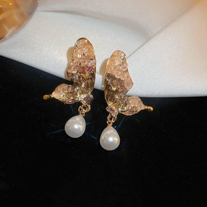 Détail de boucles d'oreilles papillon dorées avec cristaux et perles sur de la soie