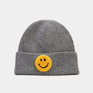 Détail du bonnet en maille grise avec écusson smiley jaune et texture côtelée