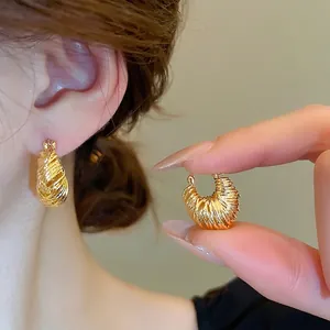 U-shaped gold plated earrings with textured ripple design shown on ear and hand