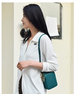 Detail of dark green canvas crossbody phone bag featuring gold zippers and layered pockets