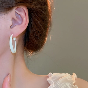Close-up of minimalist cream-colored U-shaped hoop earrings on a female model