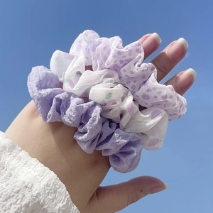Close-up of floral print and pleated purple scrunchies worn on wrist with sky background