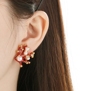 Close-up of red enamel coral earrings with pearls and gold detailing on a model