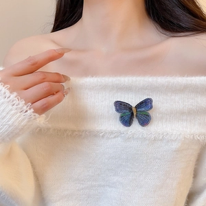 Detail of embroidered butterfly brooch with blue gradients pinned on a white sweater