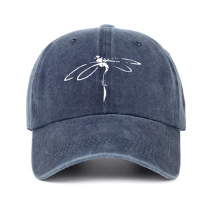 Close-up of a washed denim baseball cap featuring a white dragonfly print on deep blue fabric