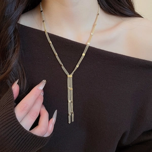 Close-up detail of golden layered tassel Y-necklace on female model wearing brown top
