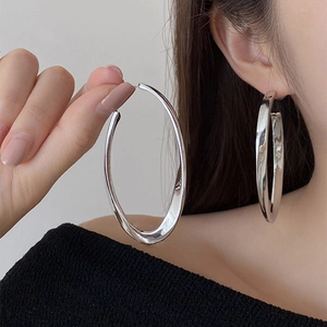 Polished silver oversized oval hoop earrings for women shown on model for scale
