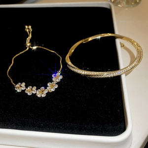 Close-up of gold-plated star flower bracelet and cross-twisted zircon bangle in a gift box