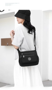 Street style shot of a multi-pocket black nylon crossbody bag with adjustable strap