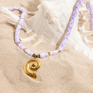Détail d'un collier en pâte polymère violette avec pendentif coquillage doré sur plage