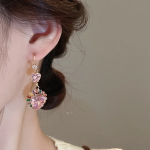 Detail of pink heart dangle earrings with gold tassels worn by a model in soft light