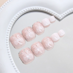 Pink press-on toenails with white ribbon bows and fine glitter on a heart mirror tray