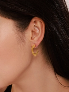 Detail of gold C-shaped sunburst earrings with beaded texture on a female model