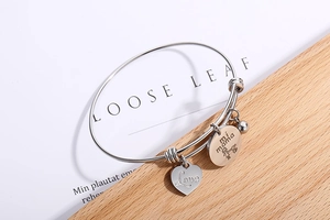 Detail of silver heart charm with Love engraving and mi mama pendant on a metal bracelet