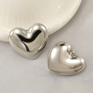 Polished silver heart-shaped stainless steel stud earrings on a textured fabric background