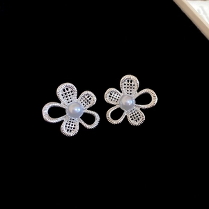 Detailed close-up of hollow flower earrings with white pearls and silver metal mesh texture