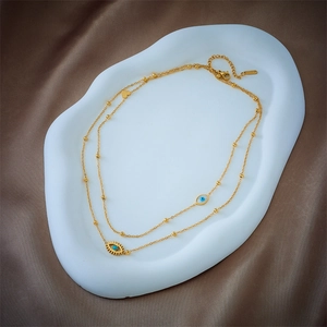 Double-layered gold necklace featuring evil eye and heart charms on a white tray