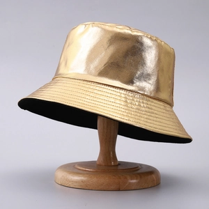 Close-up of a metallic gold PU leather bucket hat with shiny finish on a wooden stand