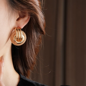 Close-up of gold woven mesh hoop earring featuring circular polished metal rings on a model