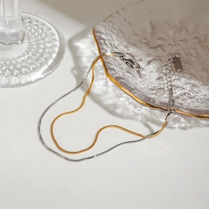 Detail view of two-tone gold and silver herringbone necklace with lobster clasp on glass