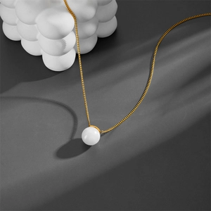 Minimalist gold chain necklace with a round pearl pendant on a dark background