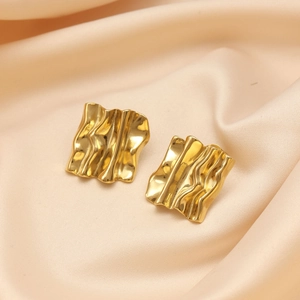 Macro shot of gold plated irregular wavy earrings on elegant silk fabric background