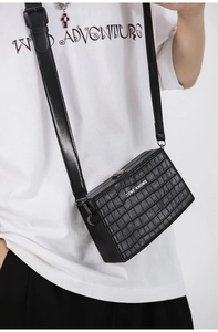 Close-up of black crocodile pattern box bag with adjustable strap and white logo text