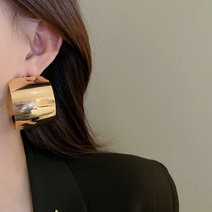 Model wearing large golden C-shaped hoop earrings with a wide polished mirror finish