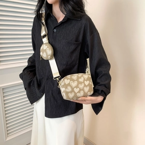 Fashionable beige crossbody bag with heart pattern and wide strap worn by model