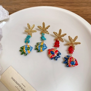 Detailed view of starfish earrings with colored stones and fish pendants on a white plate