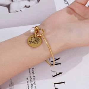 Nahaufnahme des goldfarbenen Armreifs mit Rosengravur und Perle am Handgelenk des Models