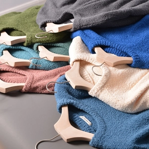 Detail view of colorful knitted sweaters layered on wooden hangers showing soft texture