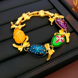 Dettaglio ravvicinato di un bracciale dorato vintage con pendenti smaltati e fiocchi