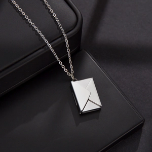 Detailed close-up of a silver envelope pendant necklace on a premium black jewelry box