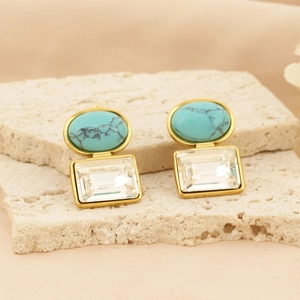 Macro shot of square gold earrings featuring turquoise and clear crystal on stone