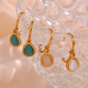 Detailed view of gold hoop earrings with teardrop cat eye stones on a glass bowl