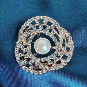 Macro detail of rose gold floral brooch with central pearl and sparkling rhinestones