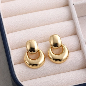 Close-up of golden geometric hollow ball and crescent earrings on cream velvet background