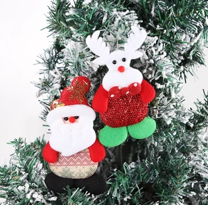Detail of fabric Santa and deer ornaments hanging on a snowy Christmas tree branch