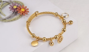 Detail shot of gold twisted cable beaded bracelet with multiple metallic charms on white