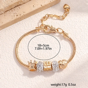 Detail of gold snake chain bracelet with crown and gift box charms on stone texture