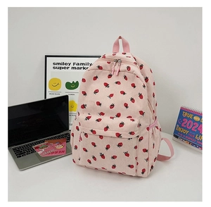 Pink corduroy backpack with strawberry print shown on a desk with a laptop and decor