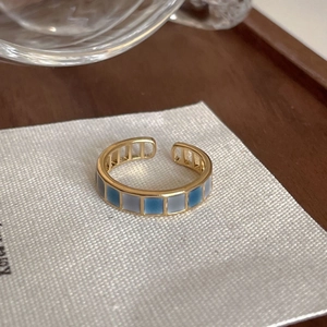 Close-up of gold ring with blue and grey checkered enamel pattern on beige fabric