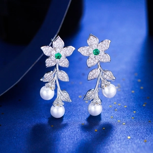 Macro detail of luxury flower earrings with green zircon and dangling white pearls