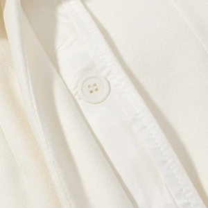 Detail of white wool coat featuring a tonal four-hole button and premium fabric texture