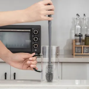 Long handle silicone cleaning brush with grey bristles washing a glass cup in kitchen